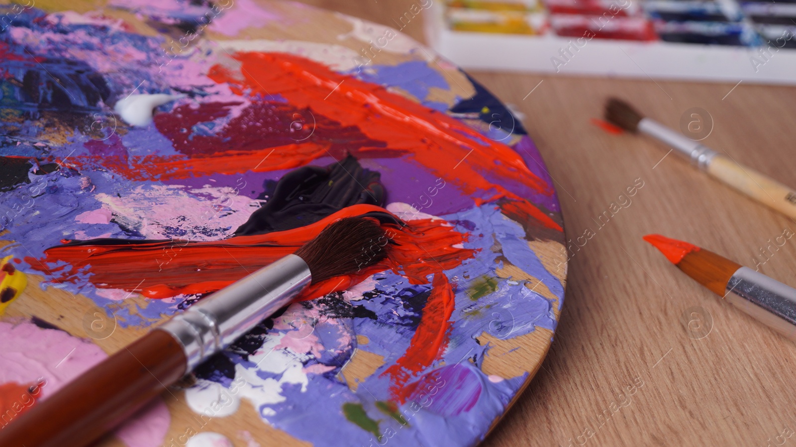 Photo of Artist's palette with mixed paints and brushes on wooden table