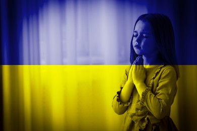 Image of Pray for Ukraine. Double exposure of little girl praying indoors and Ukrainian national flag