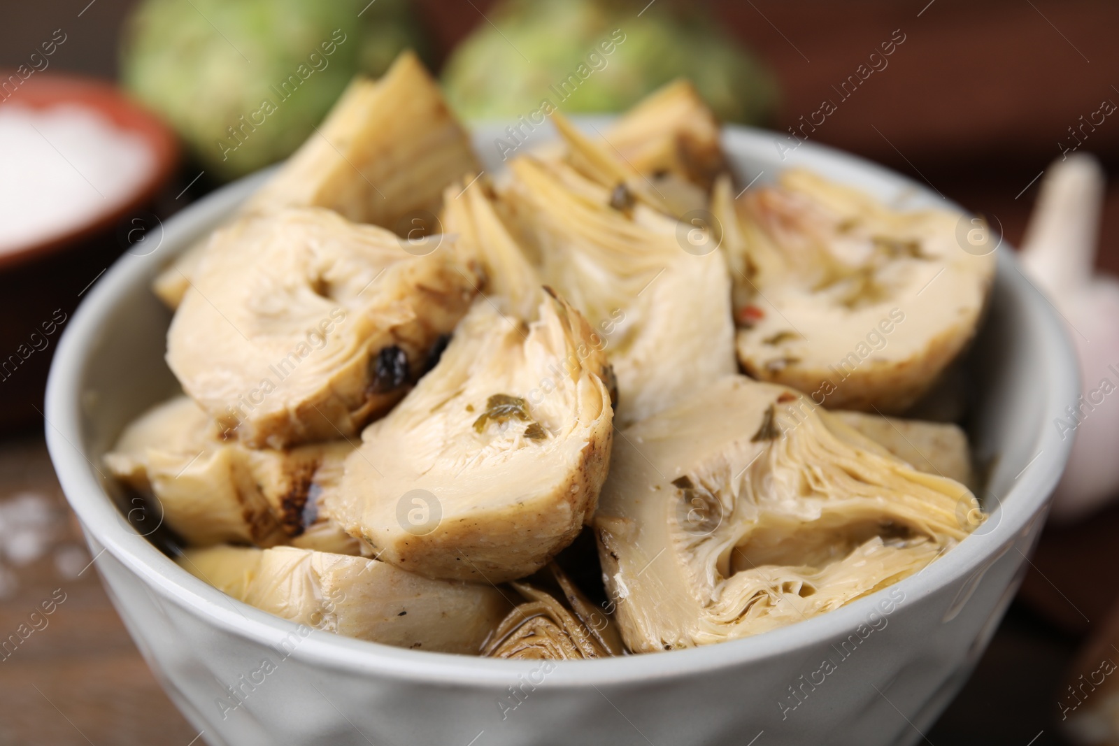 Photo of Bowl of pickled artichokes on table, closeup