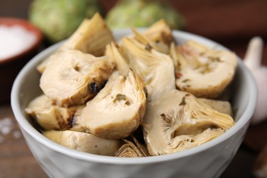 Photo of Bowl of pickled artichokes on table, closeup