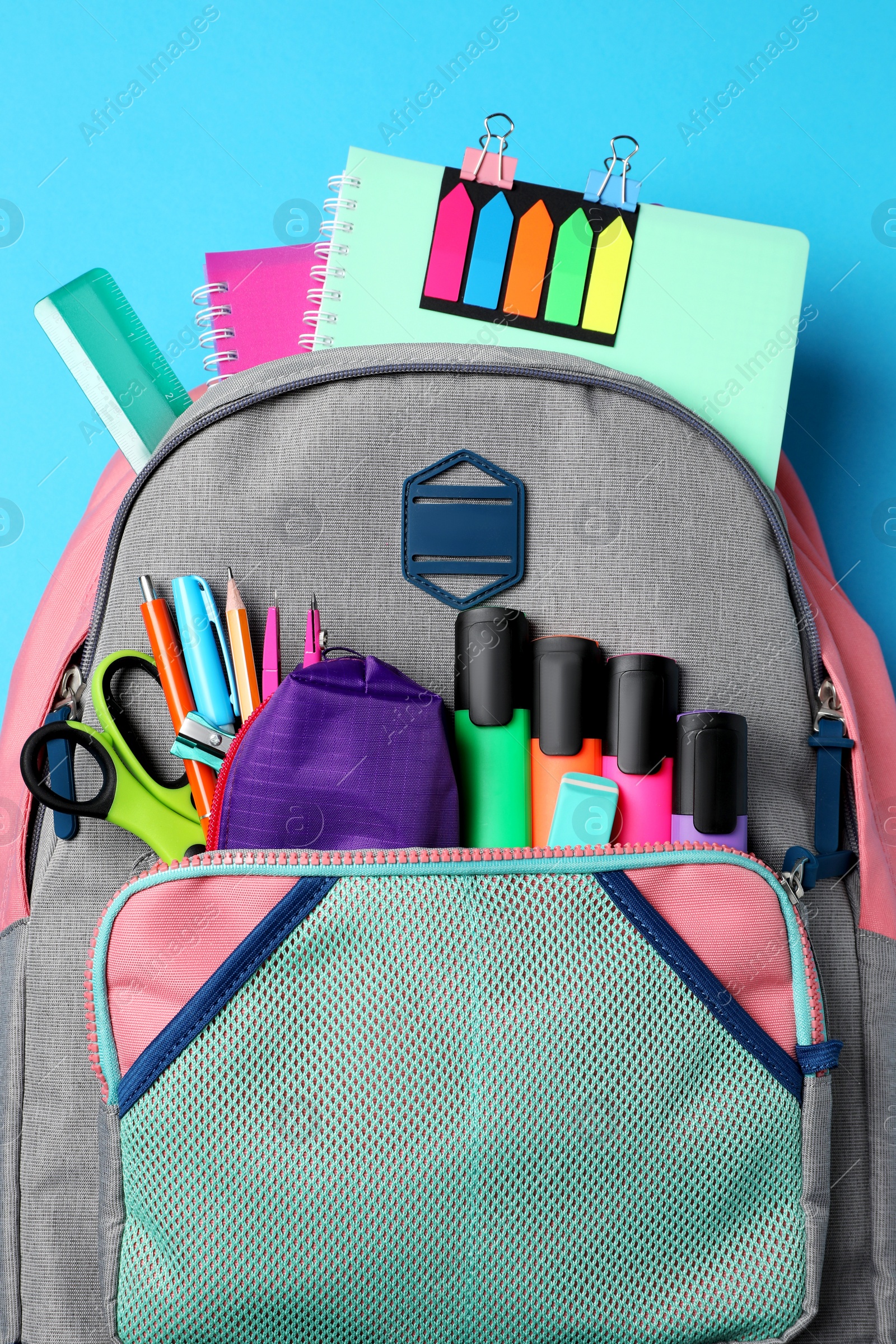 Photo of Backpack with school stationery on light blue background, top view