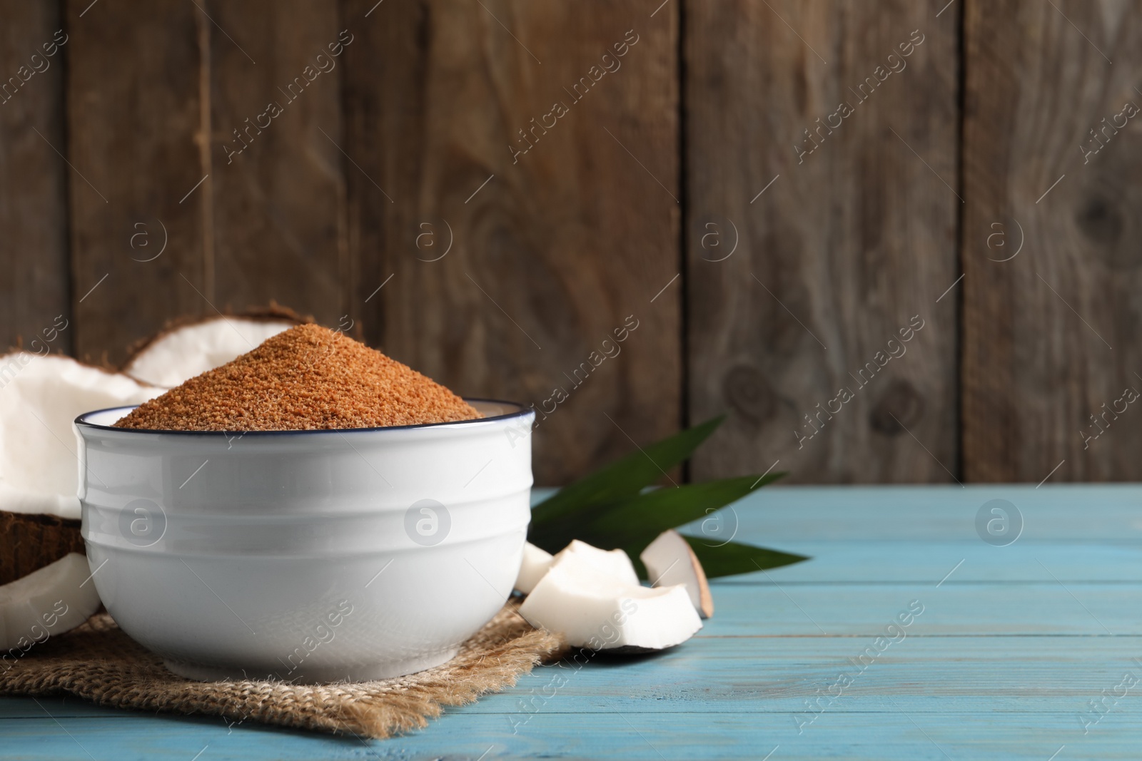 Photo of Natural coconut sugar in bowl on light blue wooden table, space for text