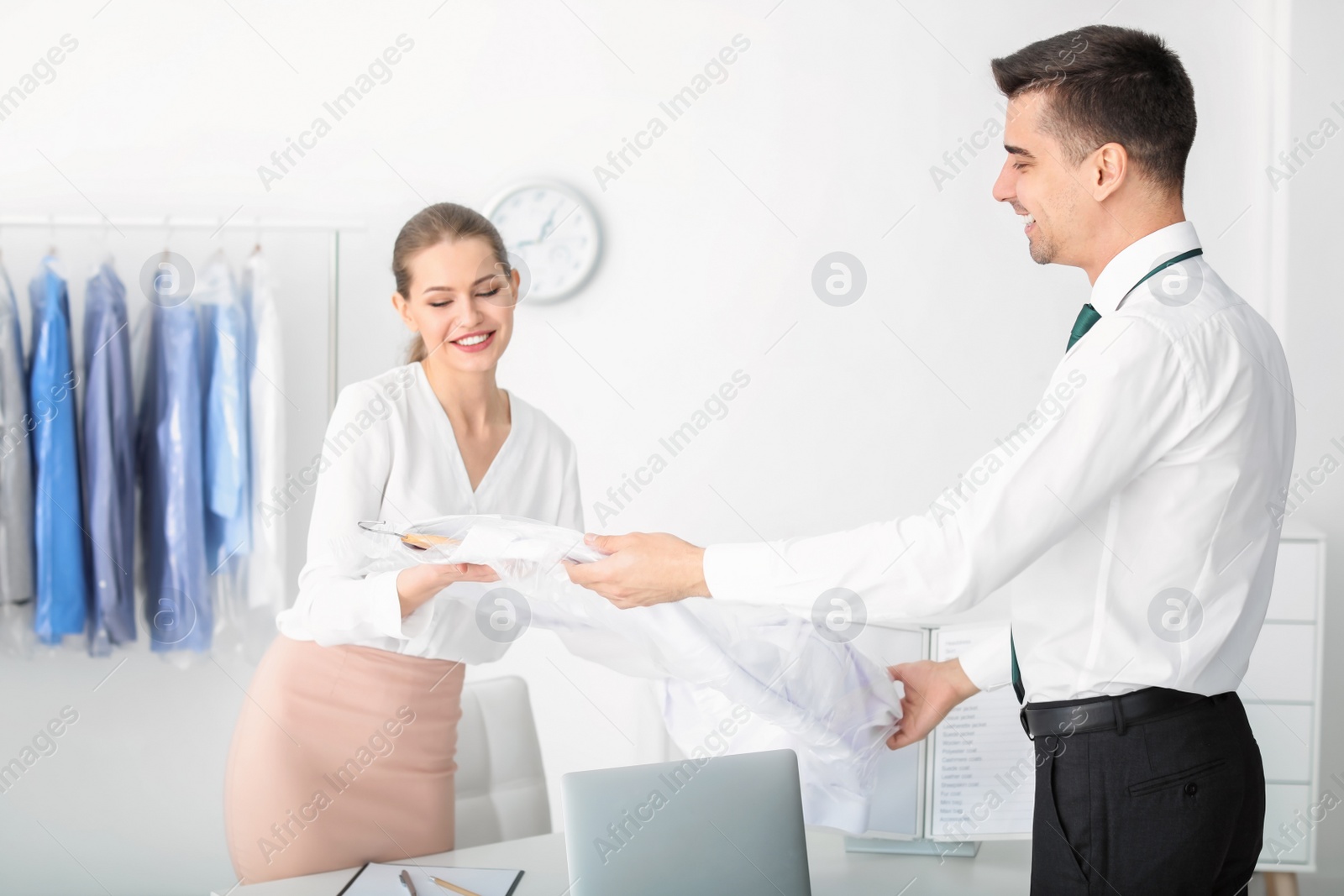 Photo of Female dry-cleaner's worker giving clothes to customer