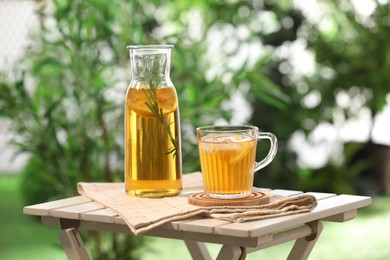 Glass bottle and cup of tasty iced tea on white wooden table against blurred background