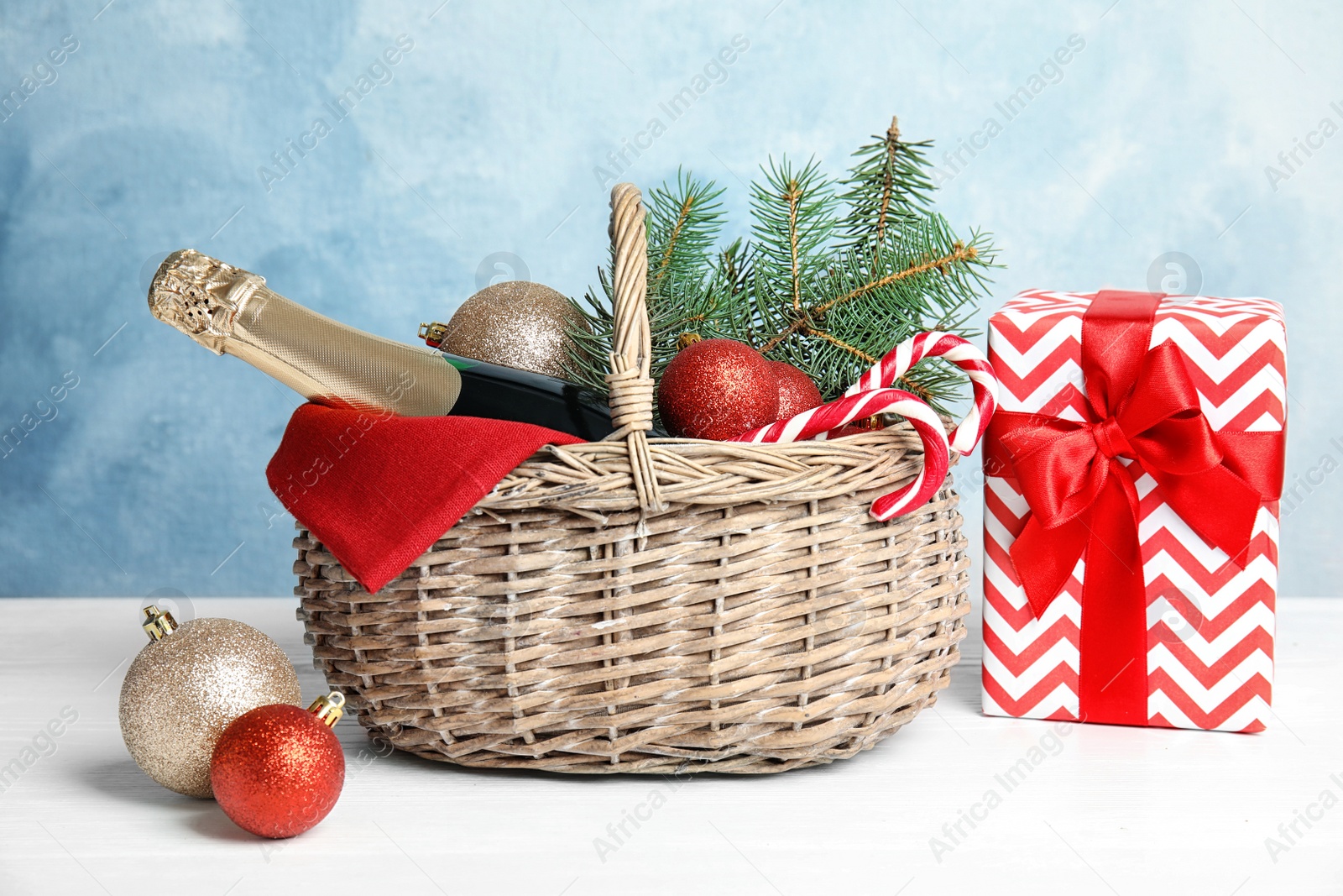 Photo of Bottle of champagne, Christmas balls with fir tree branches in wicker basket and gift on table