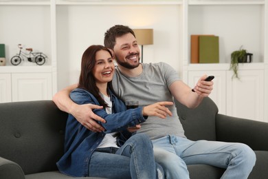 Photo of Happy couple watching show at home. Man changing TV channels with remote control