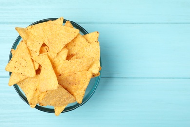 Glass bowl of tasty Mexican nachos chips on light blue wooden background, top view. Space for text