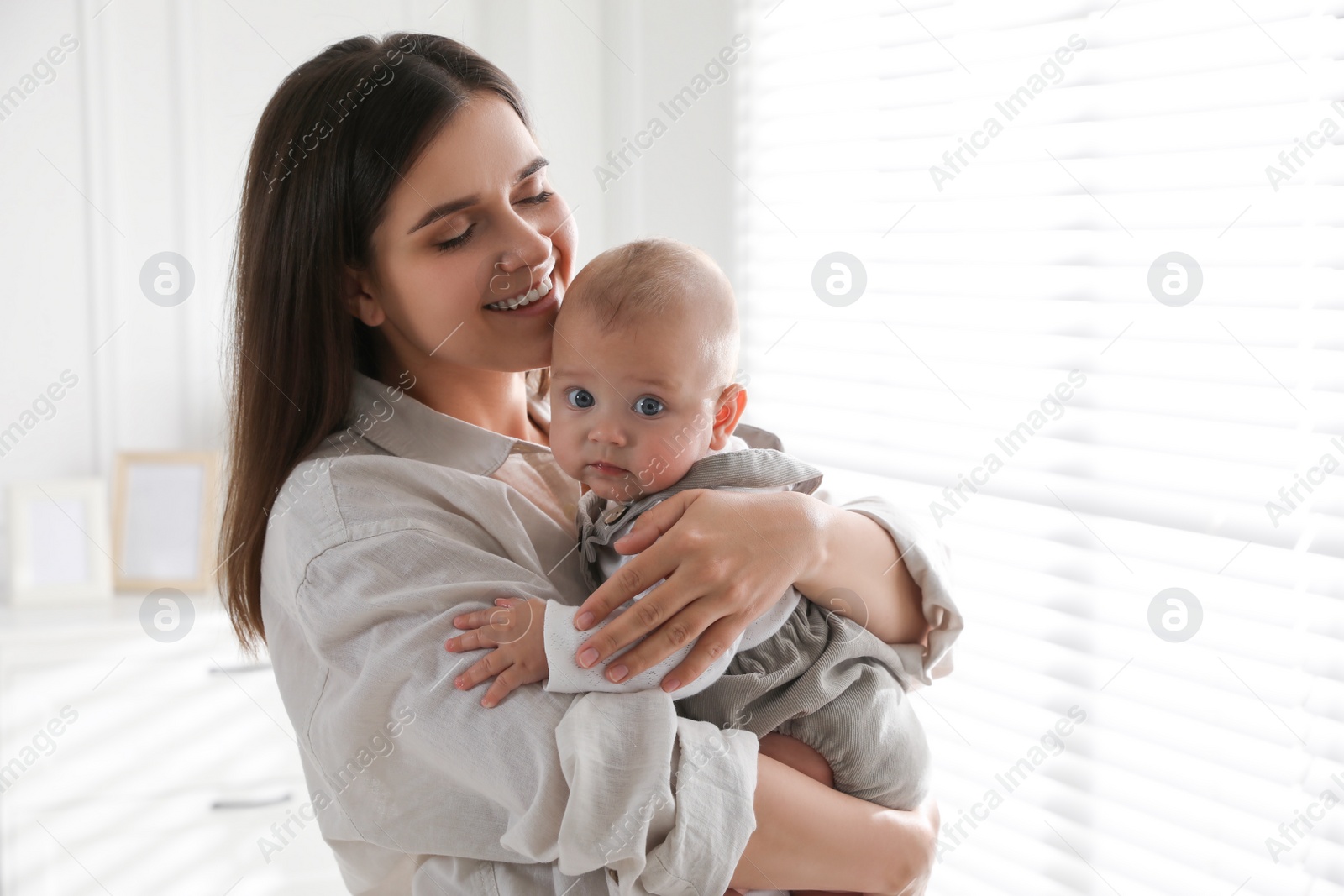 Photo of Young woman with her little baby near window at home