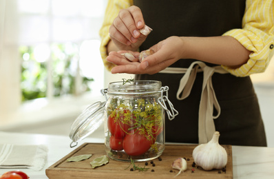 Photo of Woman putting garlic into pickling jar at table in kitchen, closeup