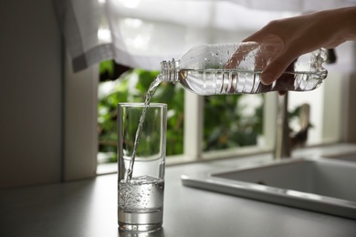 Photo of Person pouring water from bottle into glass in kitchen, closeup