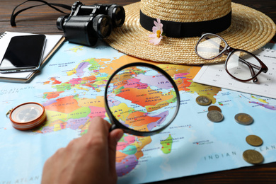 Woman looking through magnifying glass on world map at table, closeup. Travel during summer vacation