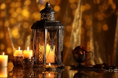 Arabic lantern, burning candles, dates and misbaha on mirror surface against blurred lights