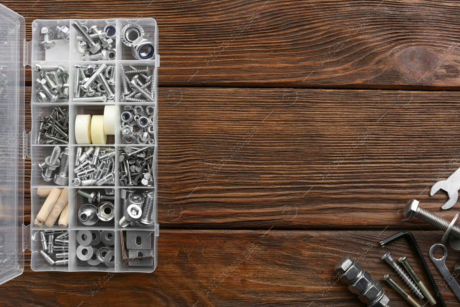 Photo of Plastic box with different furniture fittings and tools on wooden table, flat lay. Space for text