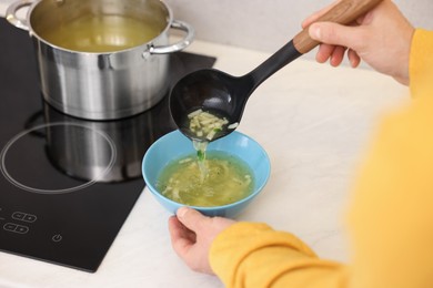 Man pouring delicious soup into bowl in kitchen, closeup