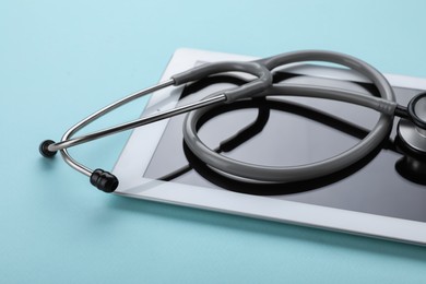 Photo of Computer tablet and stethoscope on turquoise background, closeup