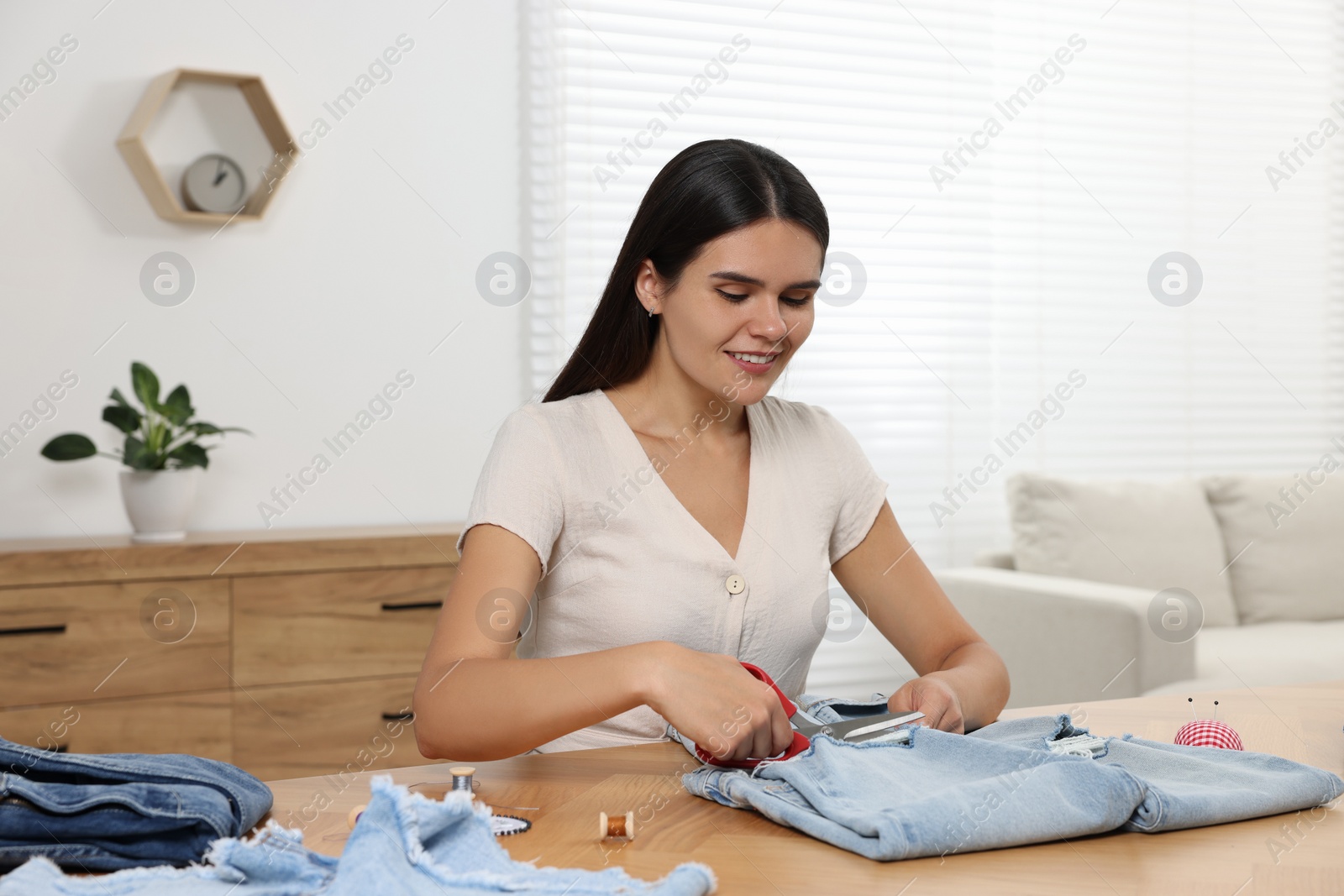Photo of Young woman cutting jeans with scissors at wooden table indoors