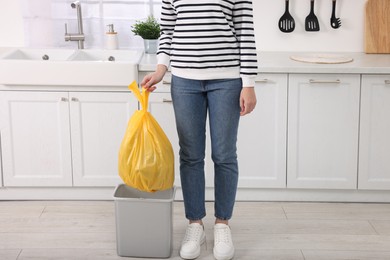 Photo of Woman taking garbage bag out of trash bin in kitchen, closeup