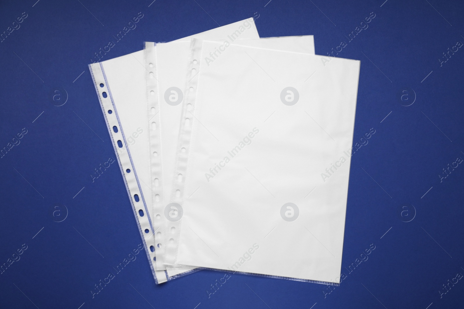 Photo of Punched pockets with paper sheets on blue background, flat lay. Space for text