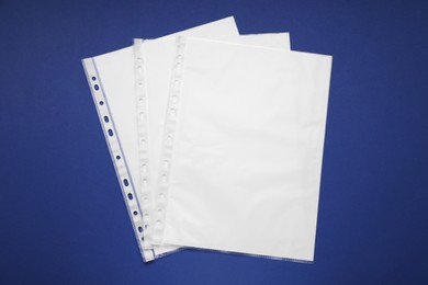 Punched pockets with paper sheets on blue background, flat lay. Space for text