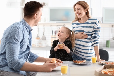 Photo of Pregnant woman and her family eating pizza in kitchen