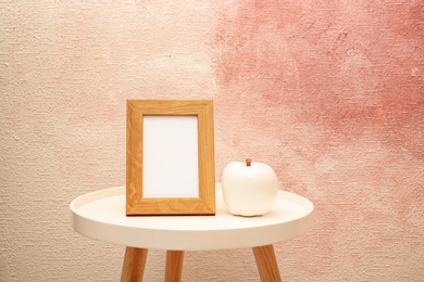 Photo of Blank frame and decorative apple figure on table near color wall. Mock up for design