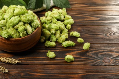 Photo of Fresh hop flowers and wheat ears on wooden table, space for text