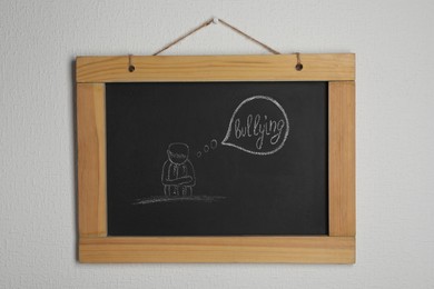 Blackboard with phrase Stop Bullying and drawn sad human on white wall