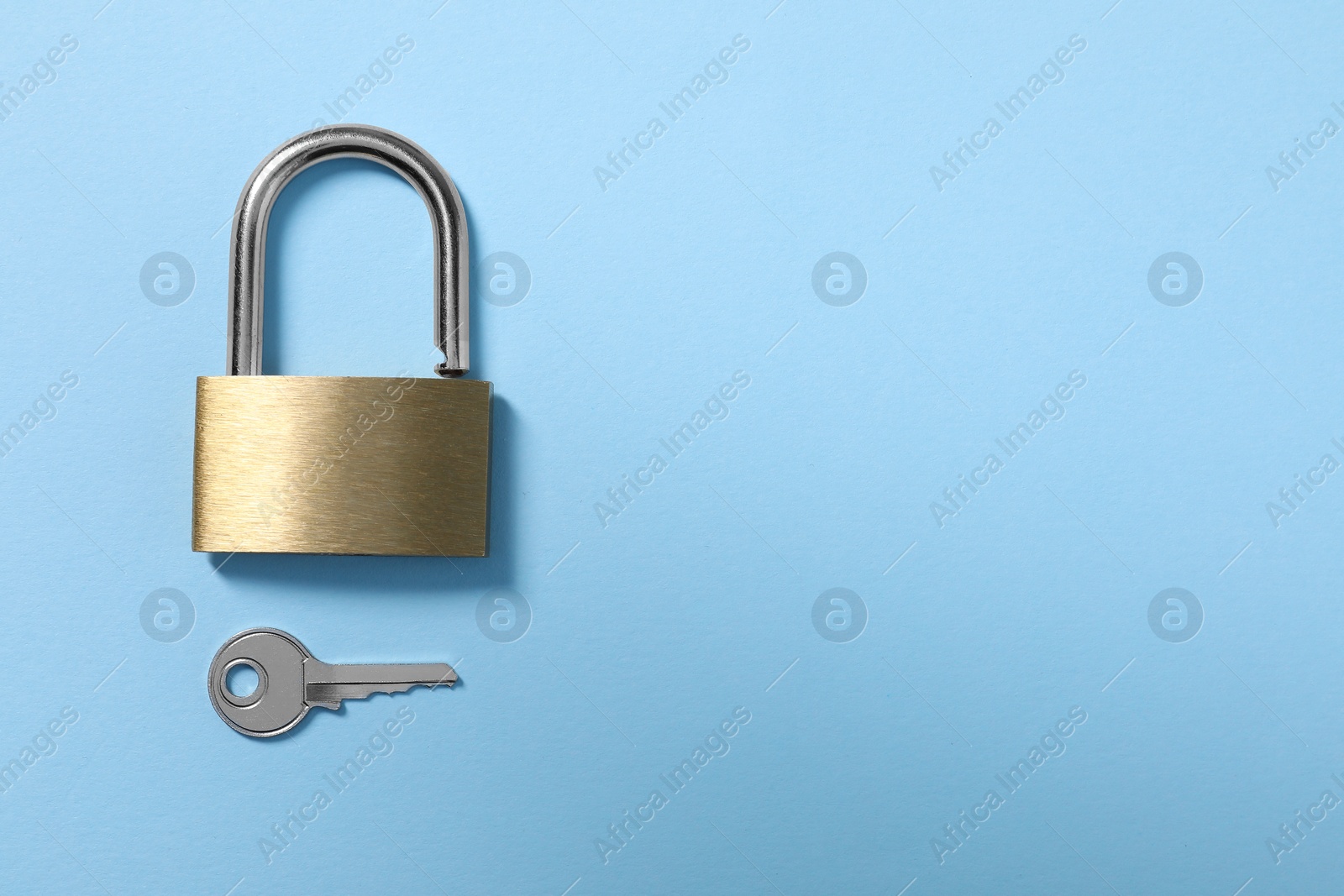 Photo of Steel padlock with key on light blue background, top view. Space for text