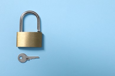 Steel padlock with key on light blue background, top view. Space for text