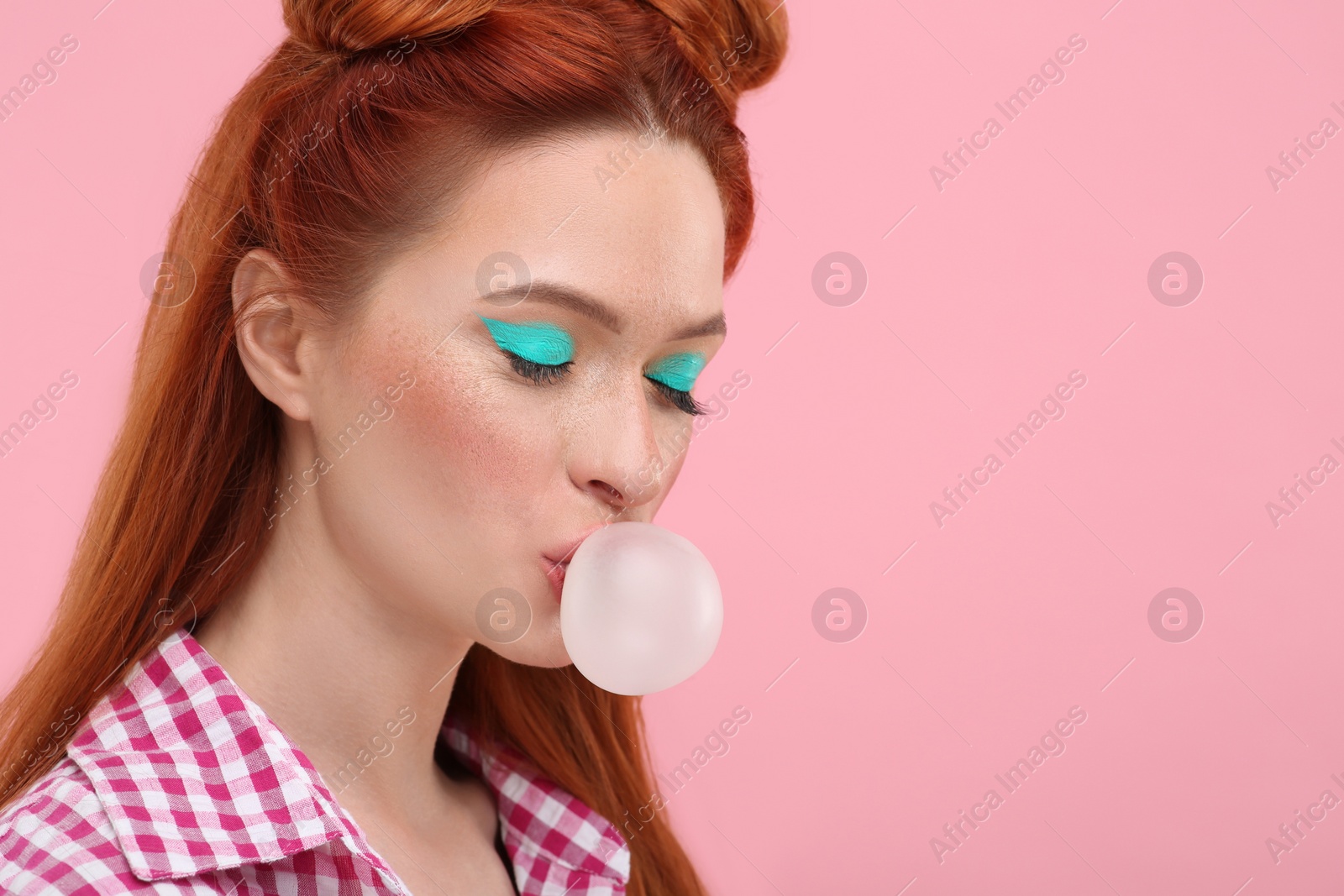 Photo of Beautiful woman with bright makeup blowing bubble gum on pink background. Space for text