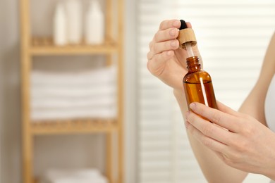 Photo of Woman with bottle of essential oil in bathroom, closeup. Space for text
