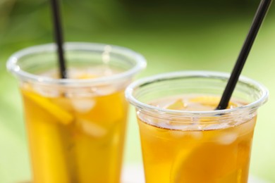 Plastic cups of tasty iced tea with lemon against blurred green background, closeup