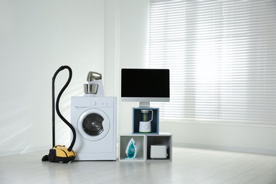 Photo of Modern vacuum cleaner and different household appliances near window indoors