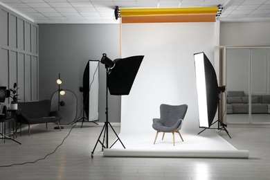 Photo of White photo background, armchair and professional lighting equipment in studio