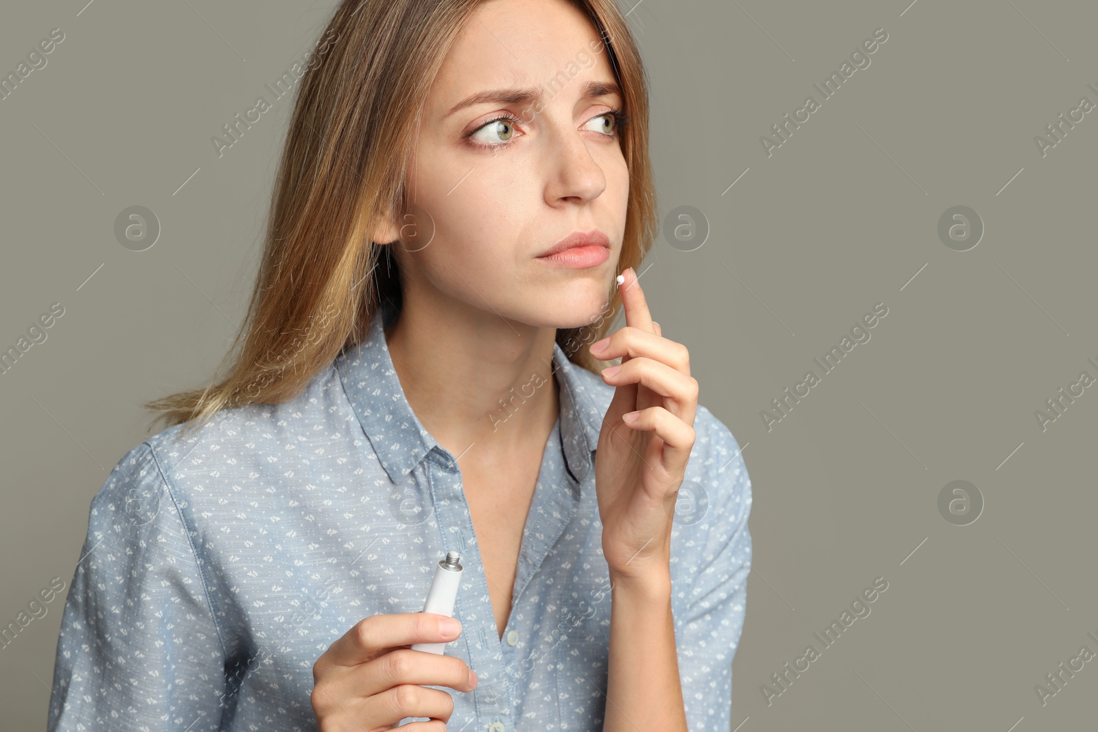 Photo of Woman with herpes applying cream onto lip against  light grey background