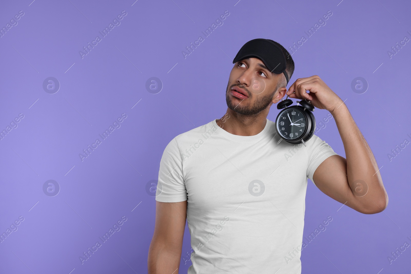 Photo of Tired man with alarm clock on violet background, space for text. Insomnia problem