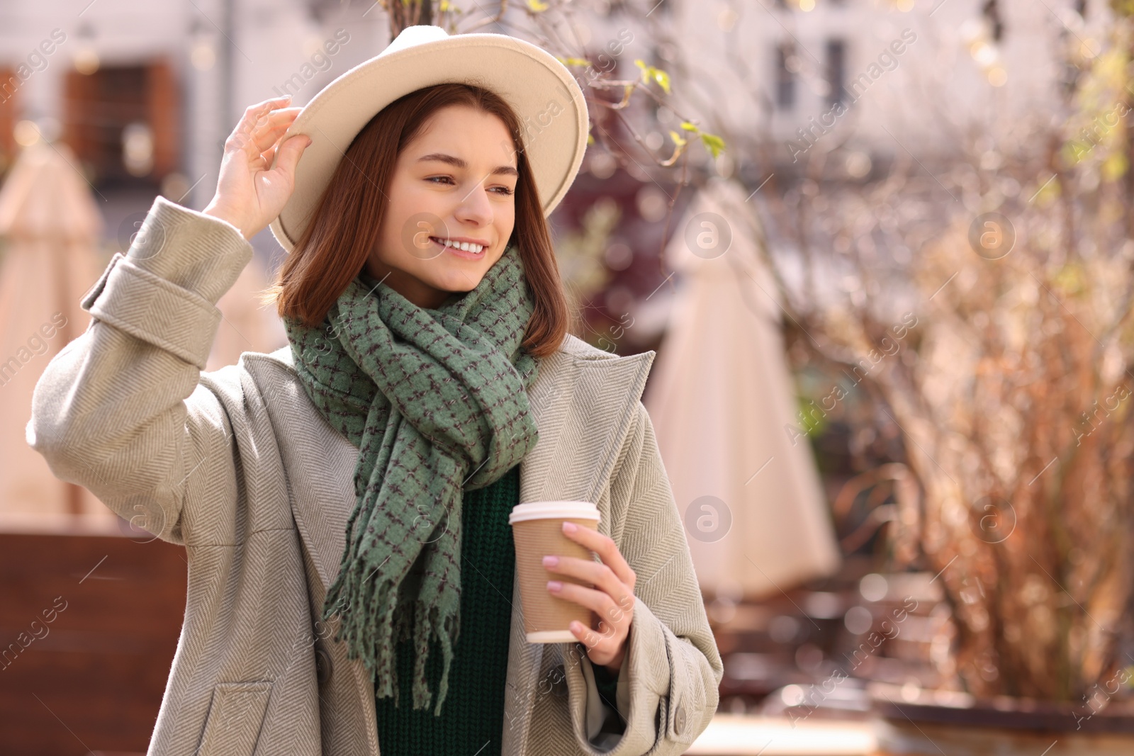 Photo of Beautiful woman in warm scarf with paper cup of coffee on city street