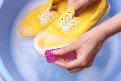 Woman washing shoe with brush in basin, closeup