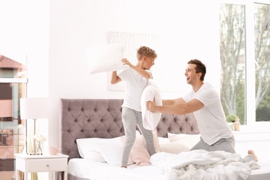 Photo of Father and son having pillow fight on bed at home