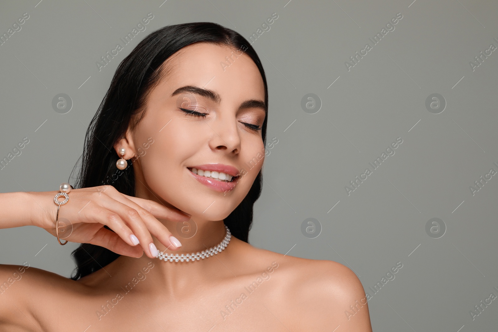 Photo of Young woman wearing elegant pearl jewelry on grey background, space for text