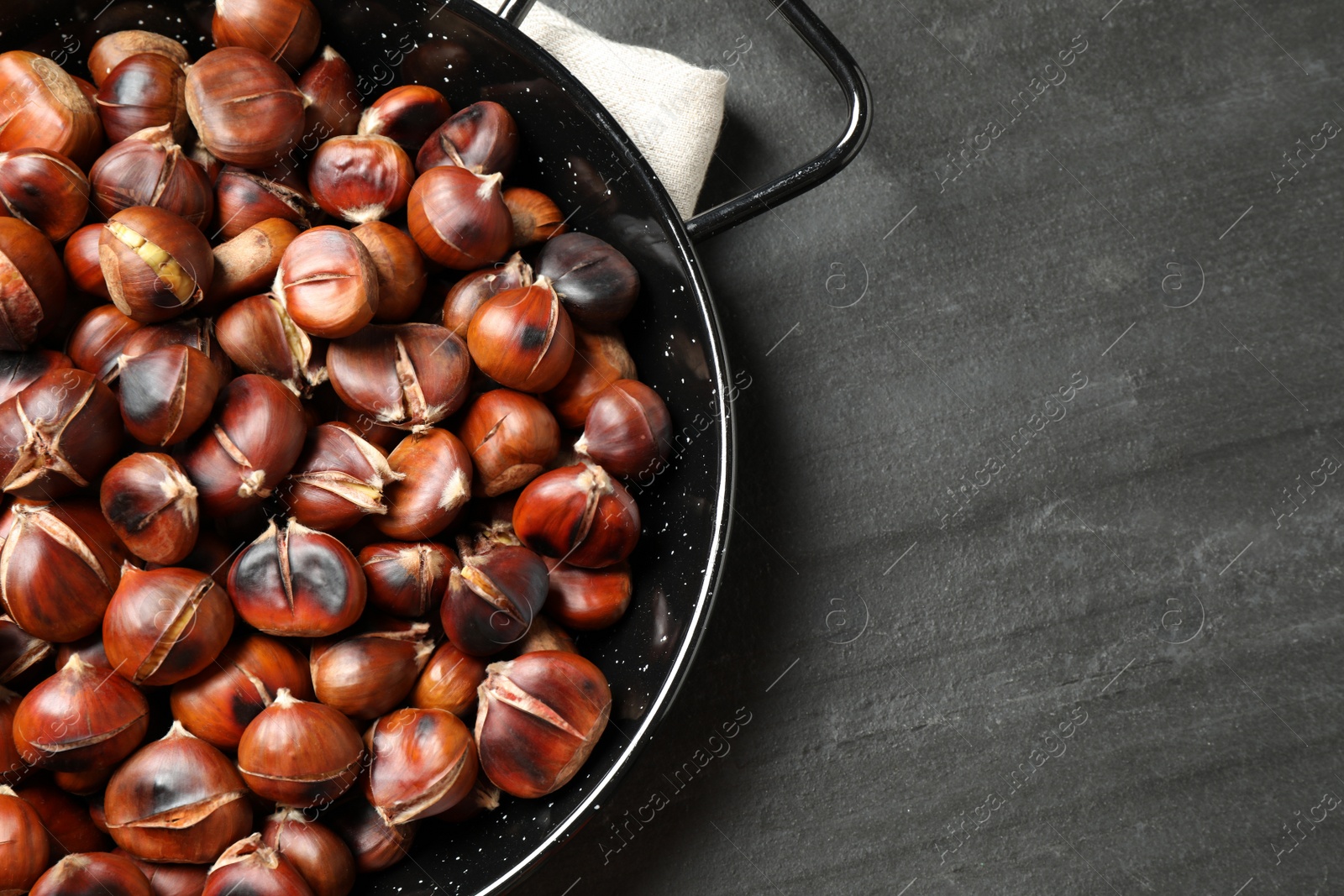 Photo of Delicious roasted edible chestnuts on black slate table, flat lay. Space for text