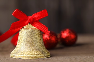 Photo of Bell with red bow on wooden table, closeup and space for text. Christmas decor