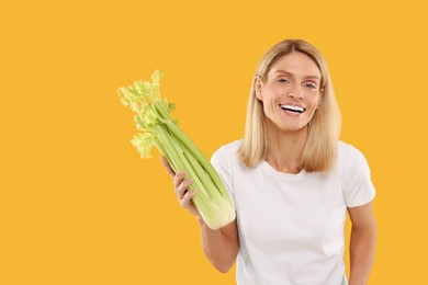 Photo of Happy woman holding fresh green celery bunch on orange background. Space for text