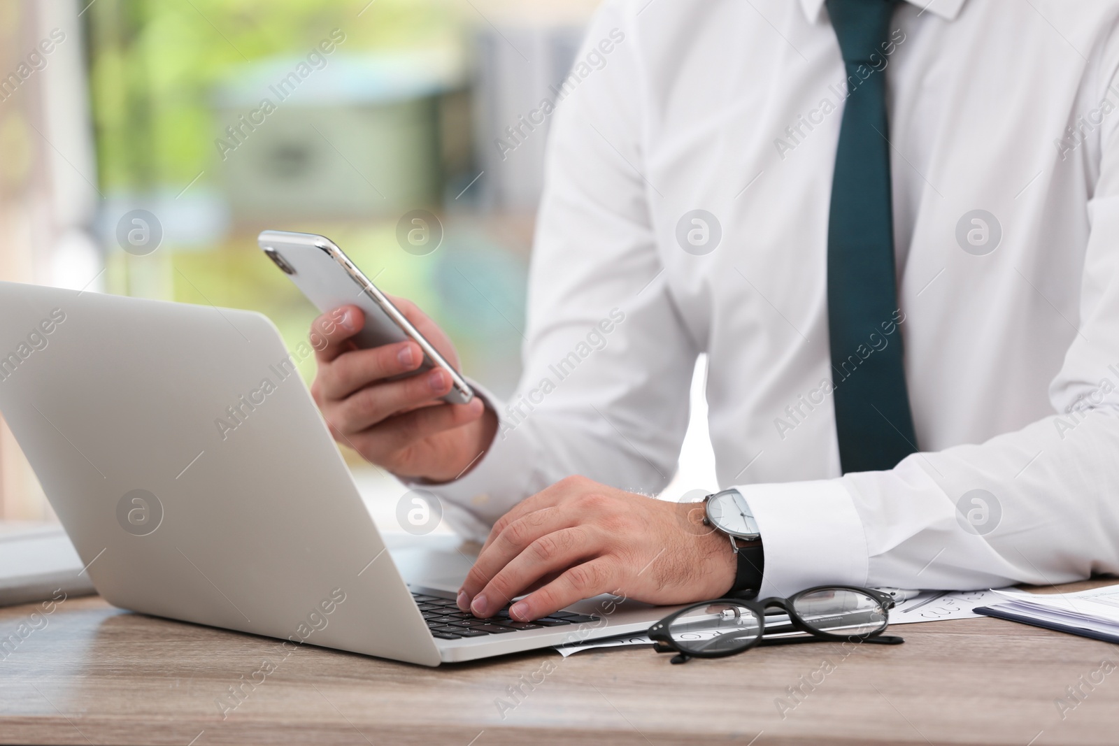 Photo of Young businessman using laptop and mobile phone at table in office