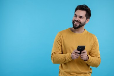 Photo of Happy young man using smartphone on light blue background, space for text