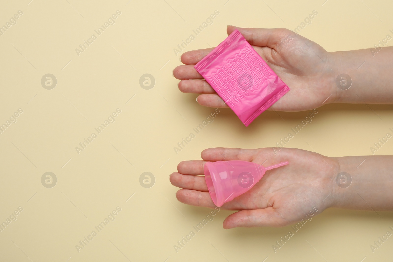 Photo of Woman holding menstrual cup and disposable pad on yellow background, top view. Space for text