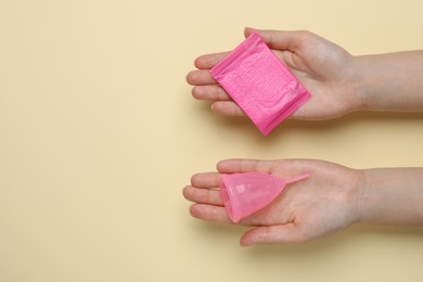 Woman holding menstrual cup and disposable pad on yellow background, top view. Space for text