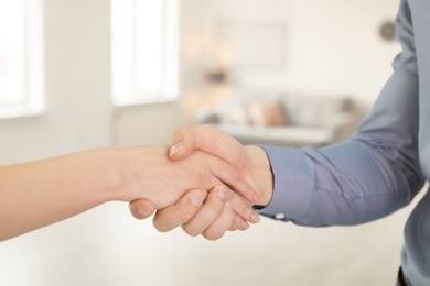 Real estate agent and young man shaking hands indoors, closeup