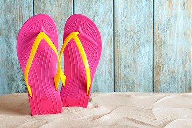 Photo of Stylish flip flops on sand near light blue wooden wall, space for text