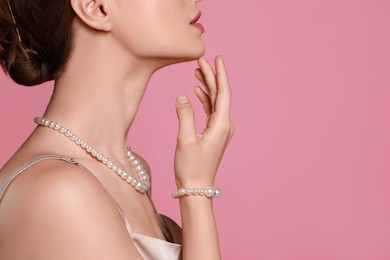 Young woman wearing elegant pearl jewelry on pink background, closeup. Space for text